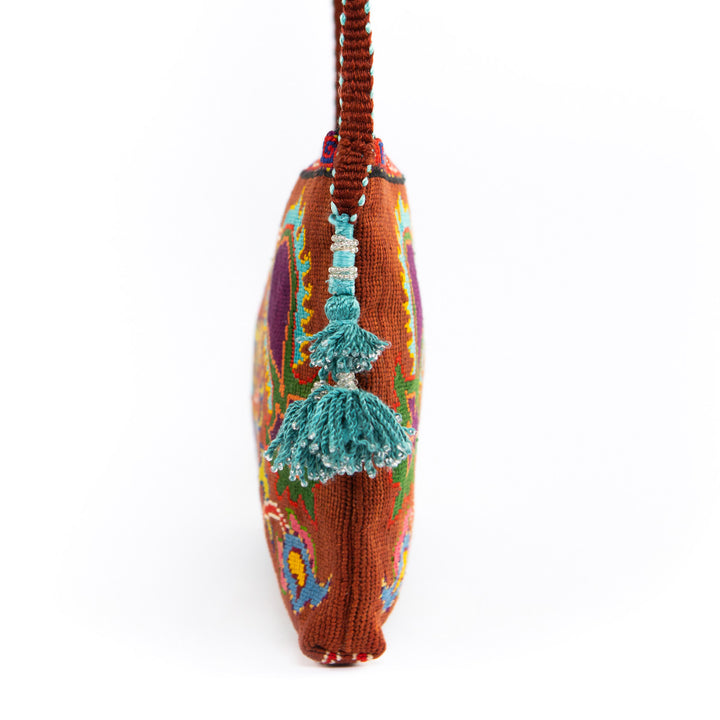 Side view of Mekhann's brown and multicoloured botanical embroidered cross-body, showcasing the bright blue tassels and the brown strap.