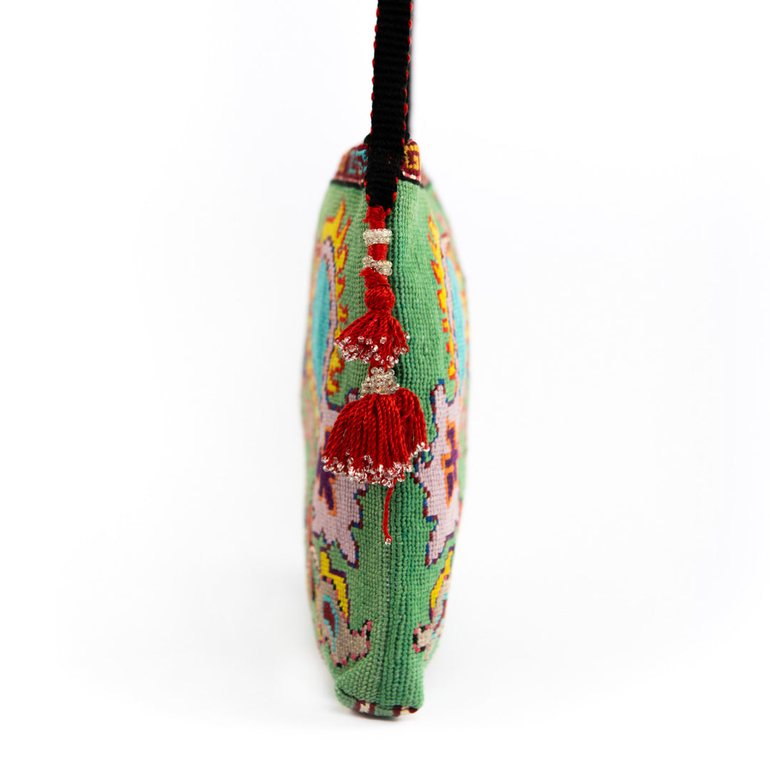Side view of Mekhann's mint botanical embroidered cross-body bag, on display is the red tassel and black and red strap.