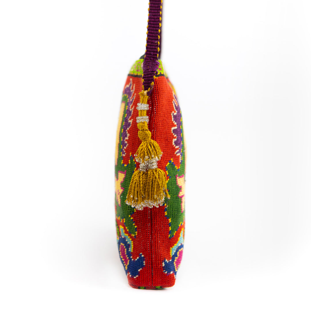 Side view of Mekhann's red botanical embroidered cross-body bag, showing off it's yellow tassel and bold purple strap.