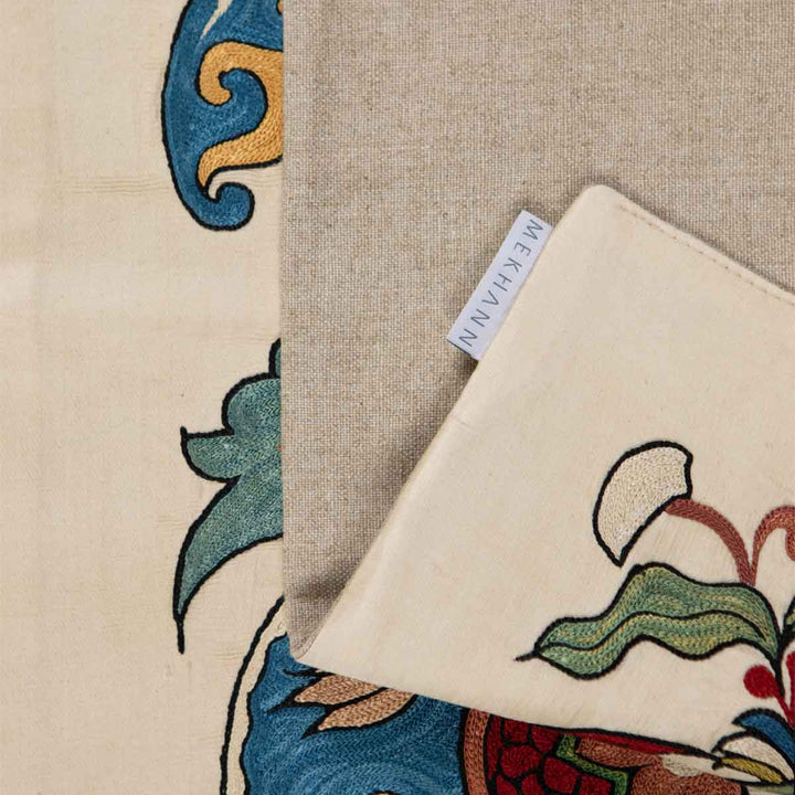Folded view of Mekhann's botanical cream petite throw, showing the back lining with the Mekhann label on display. 