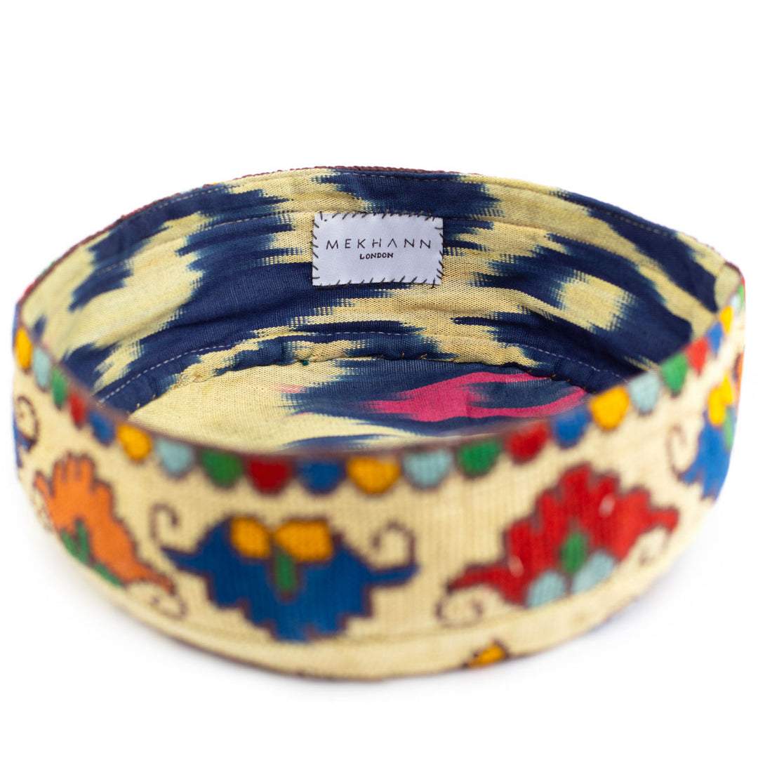 Full frame view of Mekhann's botanical cream skull cap, showcasing how the style on the ikat lining fuses seamlessly with the colours and patterns of the embroidered exterior.