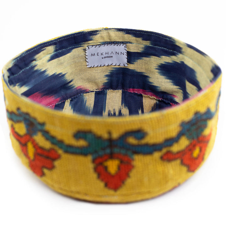 Full frame view of Mekhann's botanical yellow skull cap, showing how all the colours on the ikat lining complement the bright yellow embroidered exterior.