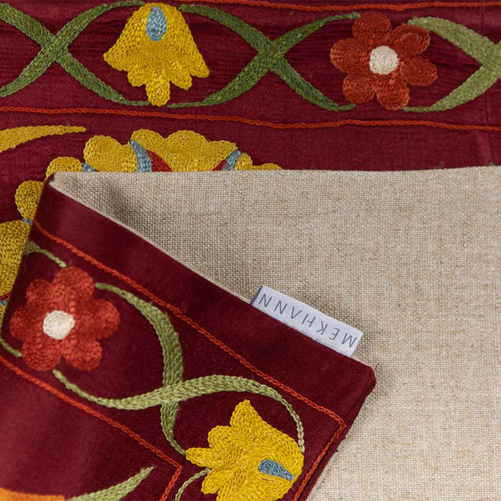 Folded view of Mekhann's maroon botanical petite throw, highlighting the botanical patterns and fabric against the maroon back lining with the Mekhann label.