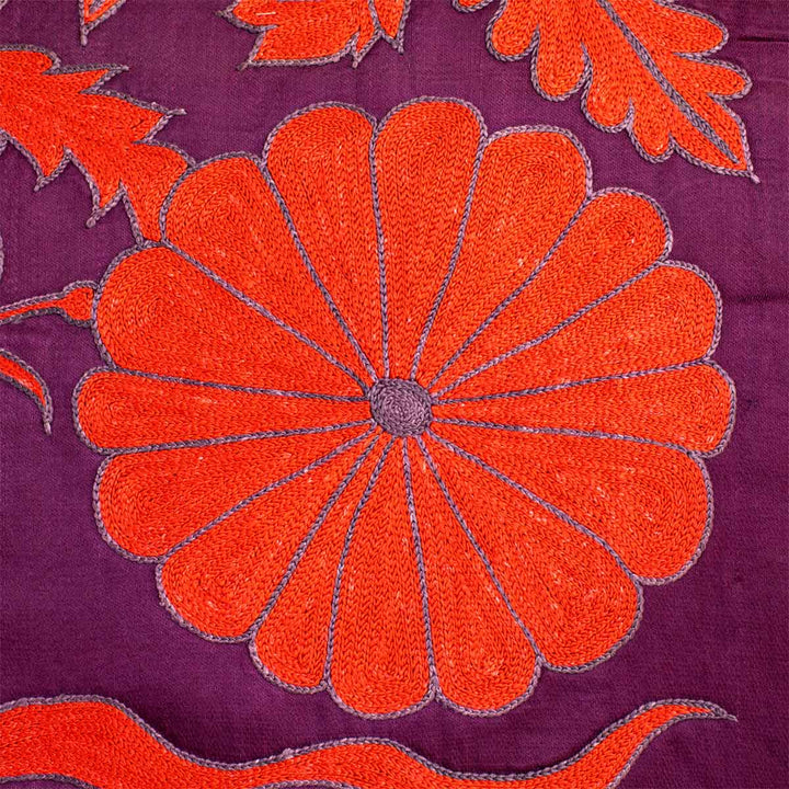 Close up view of Mekhann's royal purple botanical throw, showing how the bight orange, hand embroidered flower motif pops against the deep royal purple silk backdrop of the throw.