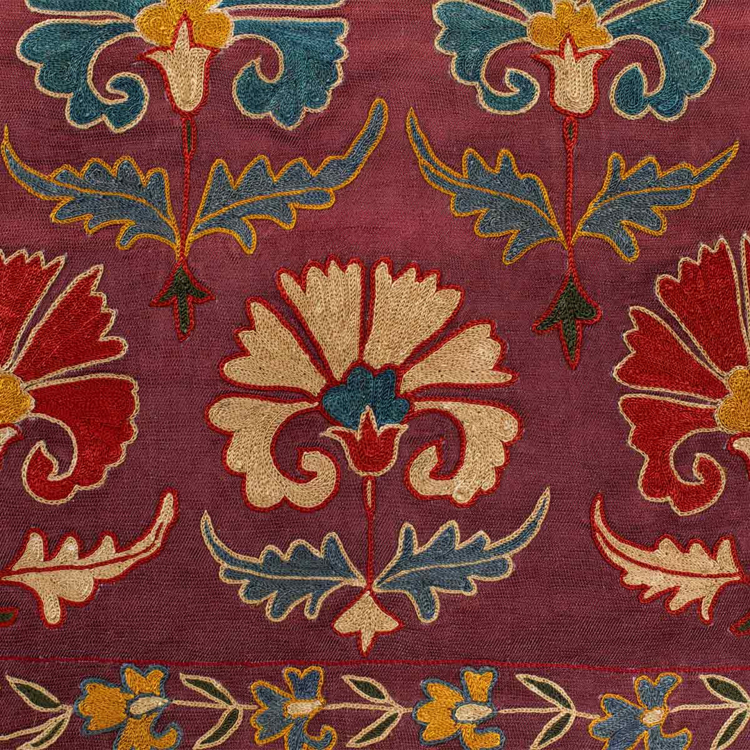 Detailed view of Mekhann's purple carnations petite throw, highlighting the elaborate embroidery and vibrant floral design that has been set on a base of purple silk fabric.