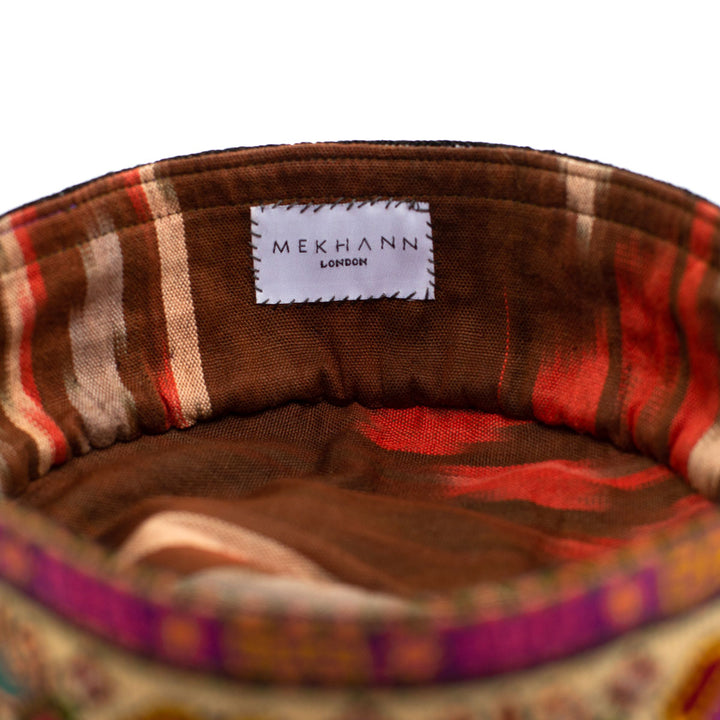 Inside view of Mekhann's multicoloured carnations skull cap, showing its brown, cream and red ikat lining. Used for both style and comfort.