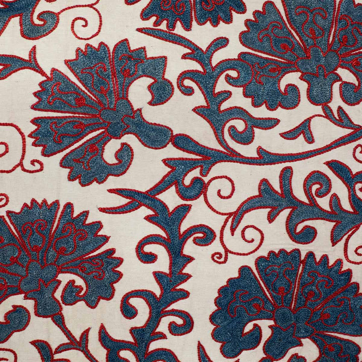 Close up view of Mekhann's cream carnations tree throw, showing the blue carnation embroidery with a bright red outlining on a base of cream coloured silk.