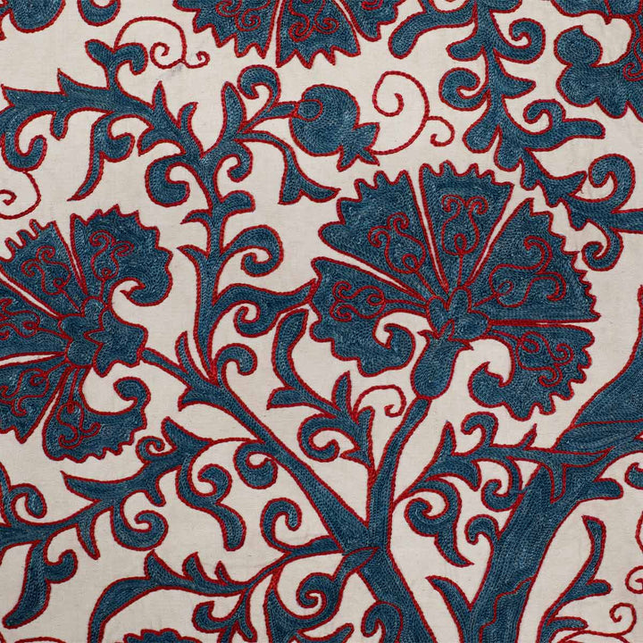 Close up view of Mekhann's cream carnations tree throw, displaying a collection of blue carnation motifs with fine detailed of red silk threads that stand out on the cream coloured silk backdrop.