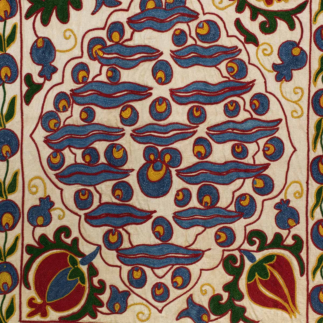 Close up view of Mekhann's cream cintamani runner, with a up close view of the silk embroidered cintamani motif in red and blue with green and yellow leafs.