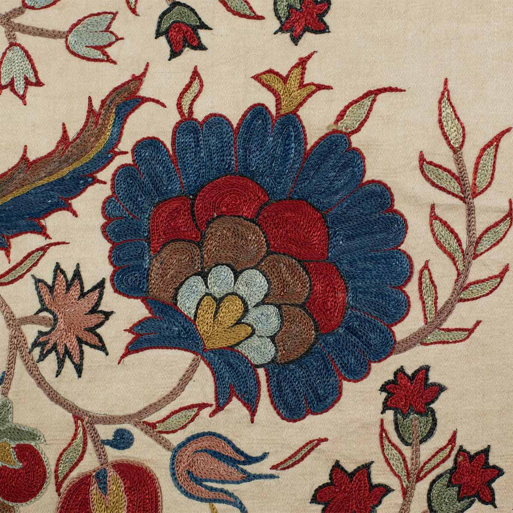 Close up view of Mekhann's cream botanical throw, where you can see all the detailing of the hand embroidery up close in blue, red and brown tones all embroidered onto a cream silk fabric.