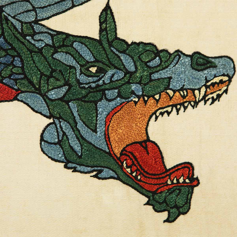 Close up view of Mekhann's black silk hand embroidered garden artwork, showcasing the attention to detail of the head of the dragon, in colours green, caramel, red and light blue, all with a black outline.