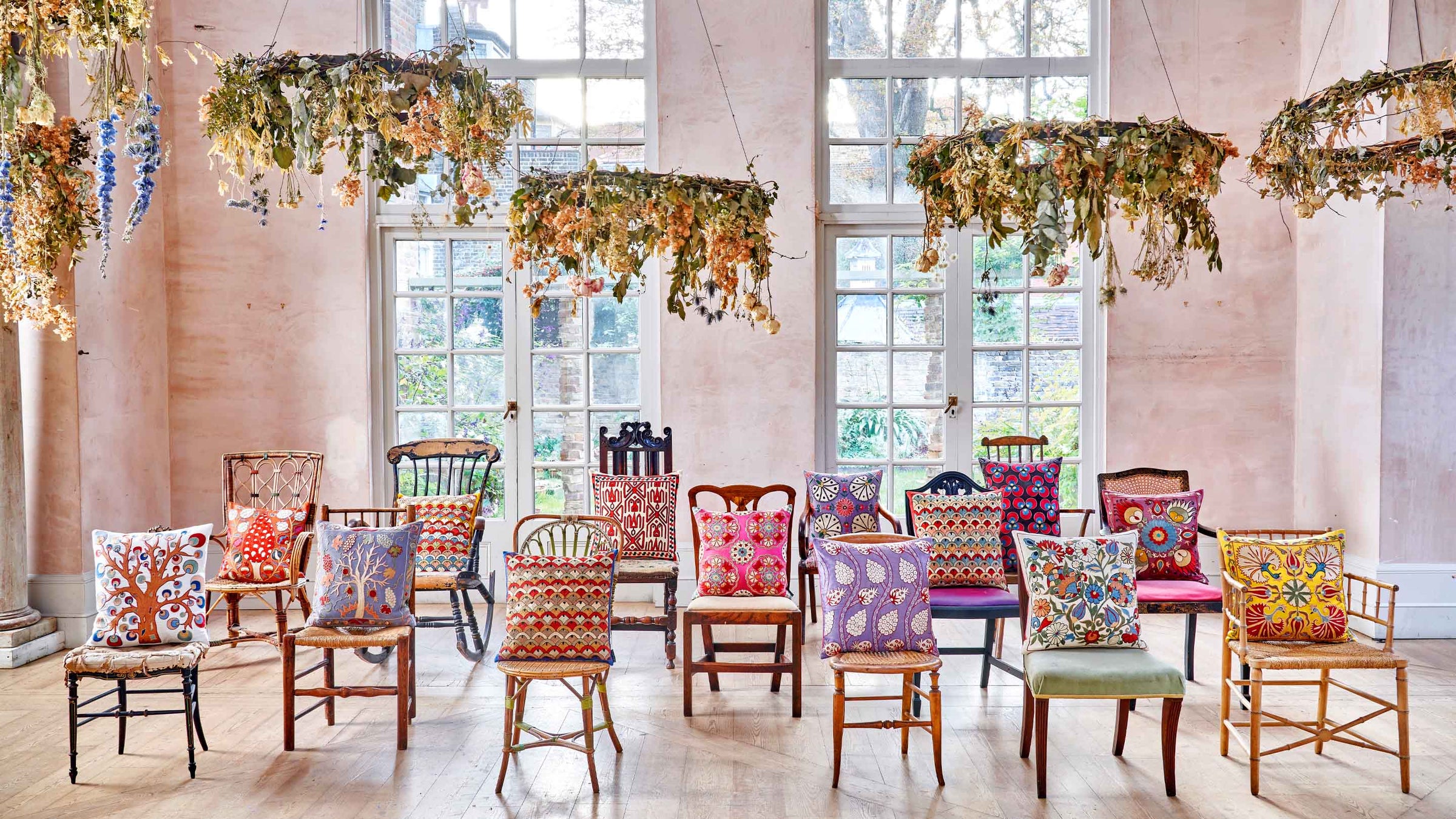 Collection of embroidered decorative cushions handcrafted from silk and velvet ikat by Mekhann, displayed on vintage chairs.