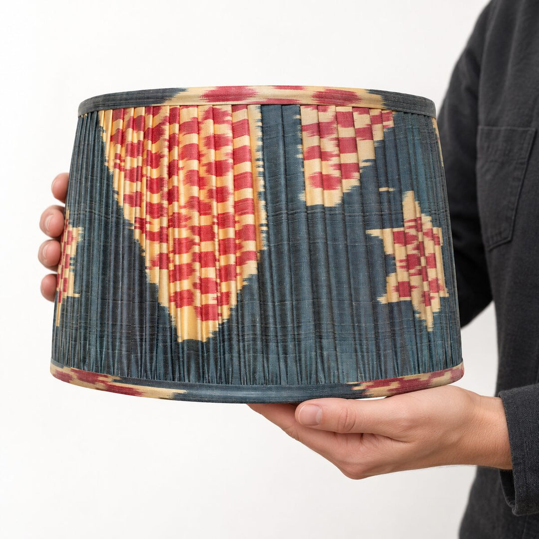 Echo Pewter silk ikat lampshade in Medium held in two hands, showing its pleated construction and pattern at scale.
