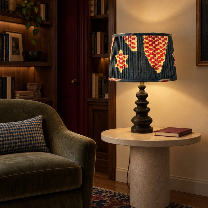 Echo Pewter silk ikat lampshade in Medium mounted on a sculptural table lamp in a warm reading room.
