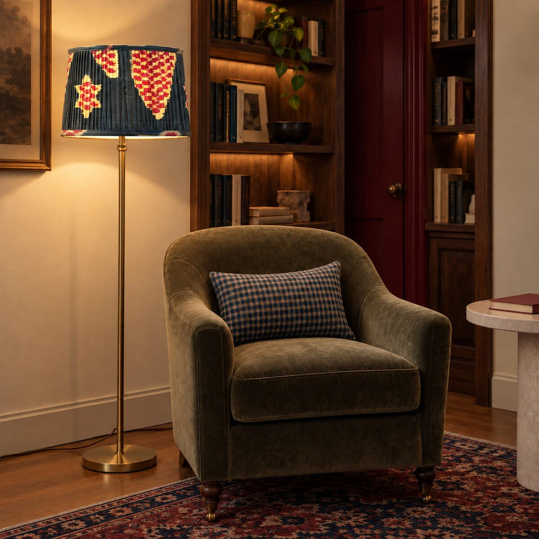 Echo Pewter silk ikat lampshade shown on a brass floor lamp beside an upholstered reading chair and fitted bookshelves.