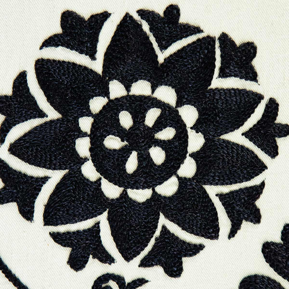 Close up view of Mekhann's white and black silk artwork with organic botanical hand embroidered shapes. Revealing a black embroidered flower motif unclose so the silk texture of the threads is fully visible and reflective of light.