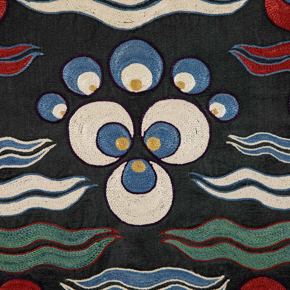 Close up view of Mekhann's black cintamani runner, with a up close view of the embroidered cintamani motif in blue, yellow and white set against the black silk background.