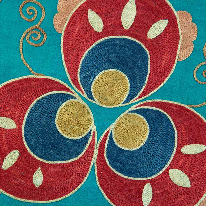 Close up view of Mekhann's floral turquoise silk embroidered artwork, focusing on the red, blue and yellow motif, which bring the intricate stitches and textures to life.
