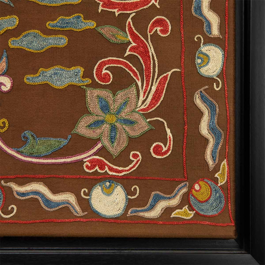 Corner view of Mekhann's brown silk peacock artwork, where we can see the corner of the black frame and where it meets the embroidered brown artwork.