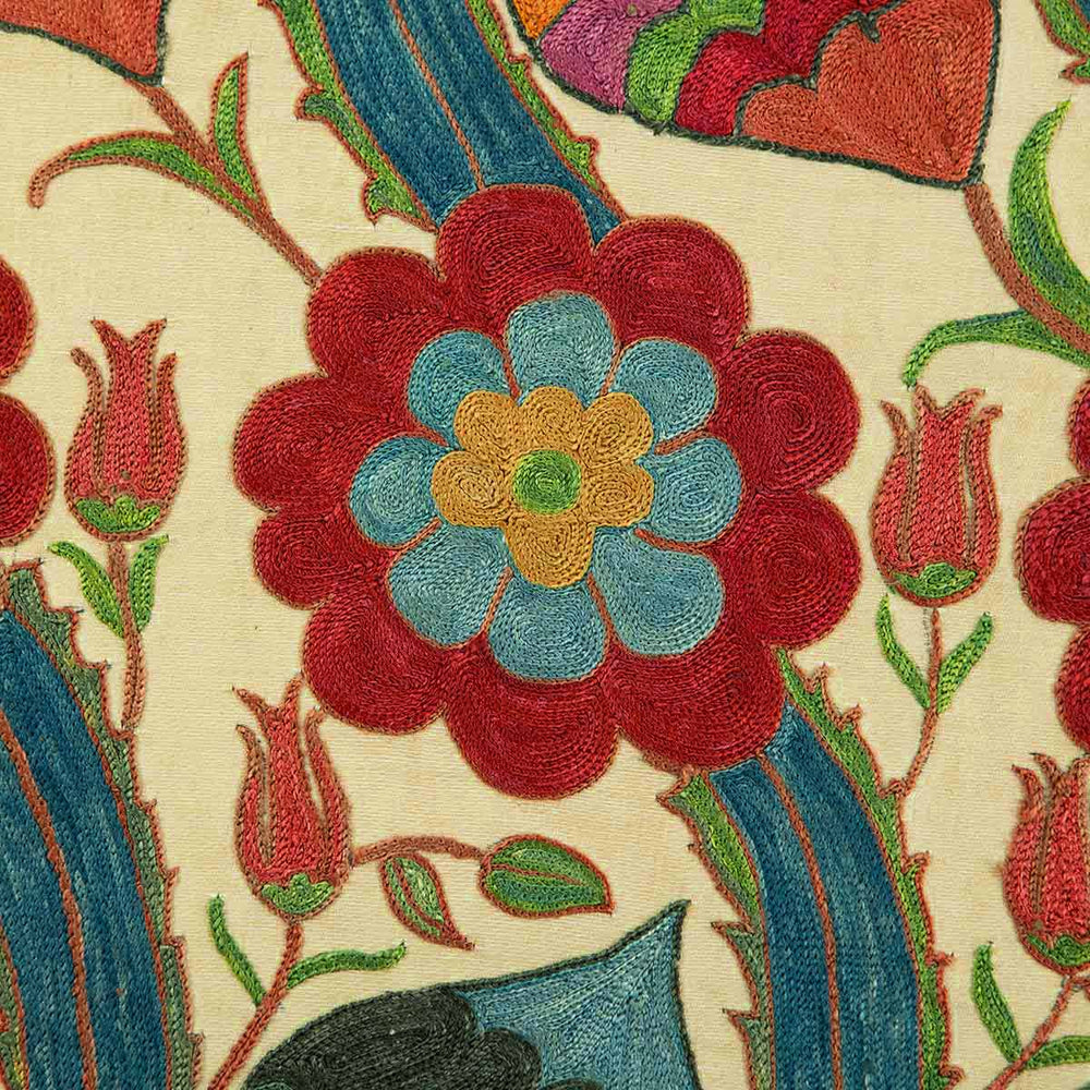 Close up view of Mekhann's cream silk vines artwork, focusing on a flower motif hand embroidered in light blue, yellow and red silk yarns.