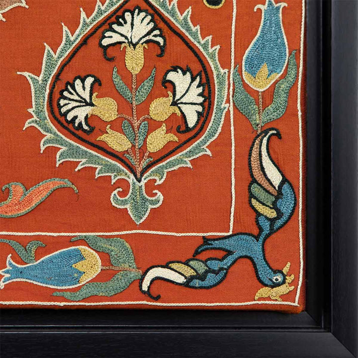 Corner view of Mekhann's maroon silk embroidered artwork, showing the  corner of the black frame and the corner of the artwork where we can see a small blue bird.