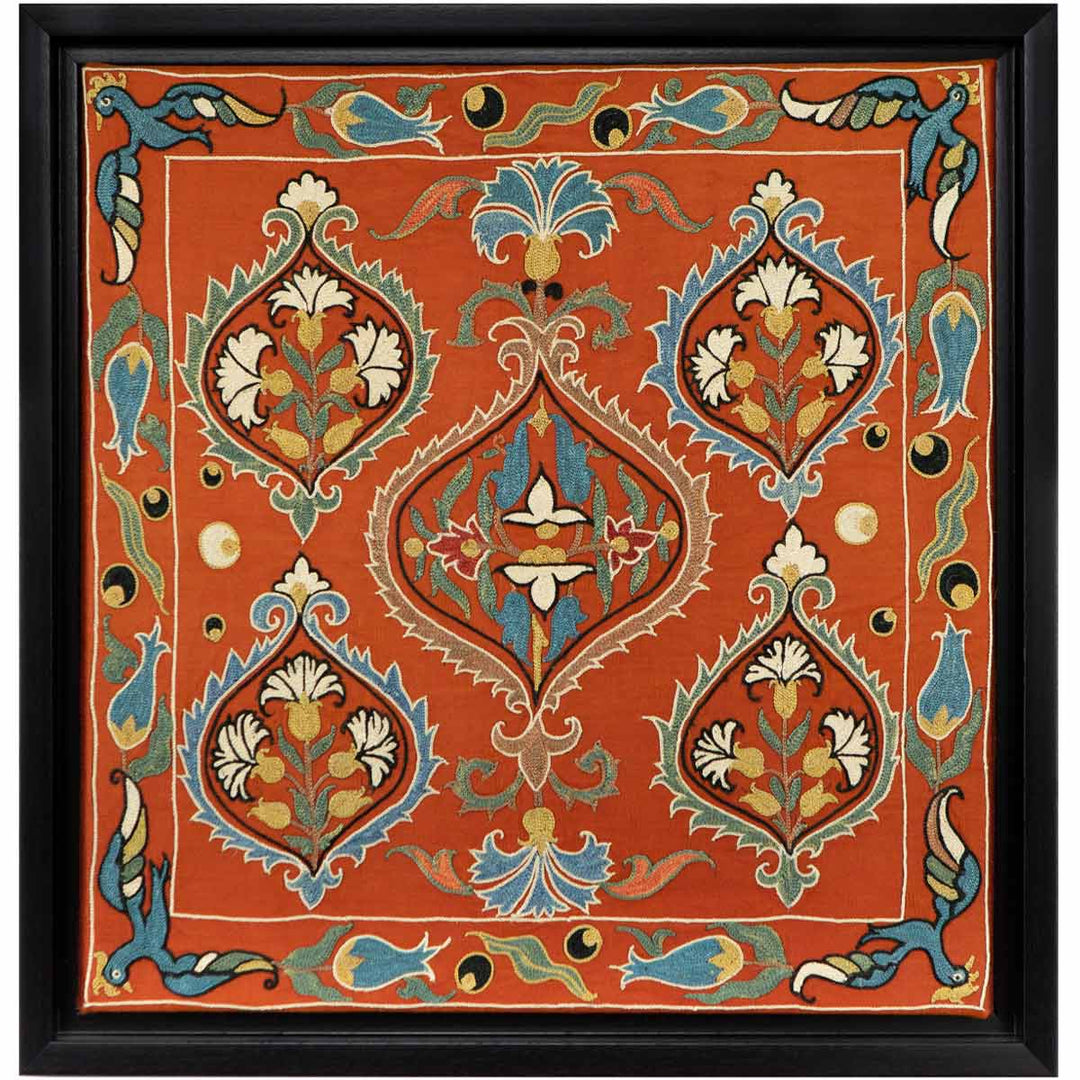 Front view of Mekhann's maroon silk embroidered artwork, featuring a silk maroon canvas adorned with symmetrical designs and flourishes in a palette of light yellow, blue, and cream, all within a black frame.