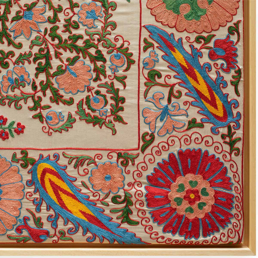 Corner view of Mekhann's cream and multicoloured silk artwork featuring a collection of floral and botanical embroidered details. Showing where the light oak frames meeting the silk artwork.