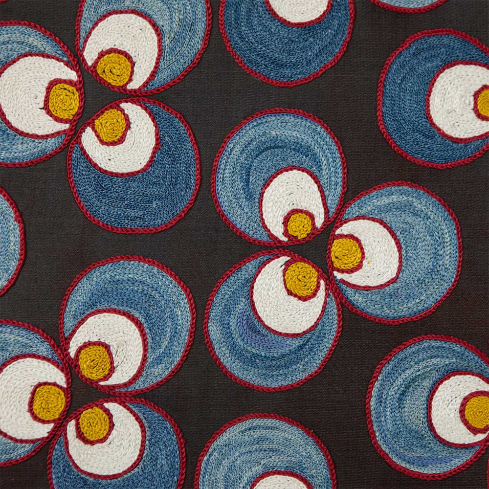 Close up view of Mekhann's black silk cintamani artwork, showcasing the blue, yellow and cream patterns closer, where we can see the delicate red outline embroidery.