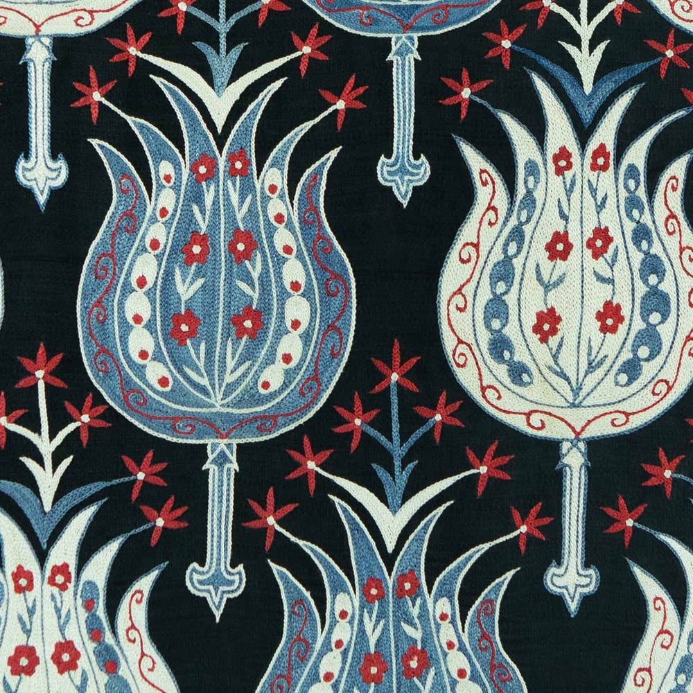 Close up view of Mekhann's black silk hand embroidered garden artwork, showing side by side one blue embroidered flower and one white embroidered flower, both of the have small red flowers within the, and also growing out of them.
