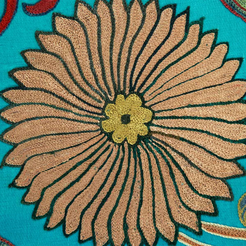 Close up view of Mekhann's hand embroidered, turquoise silk artwork, a close view of the beige embroidered flower with black outlines against the turquoise silk background.