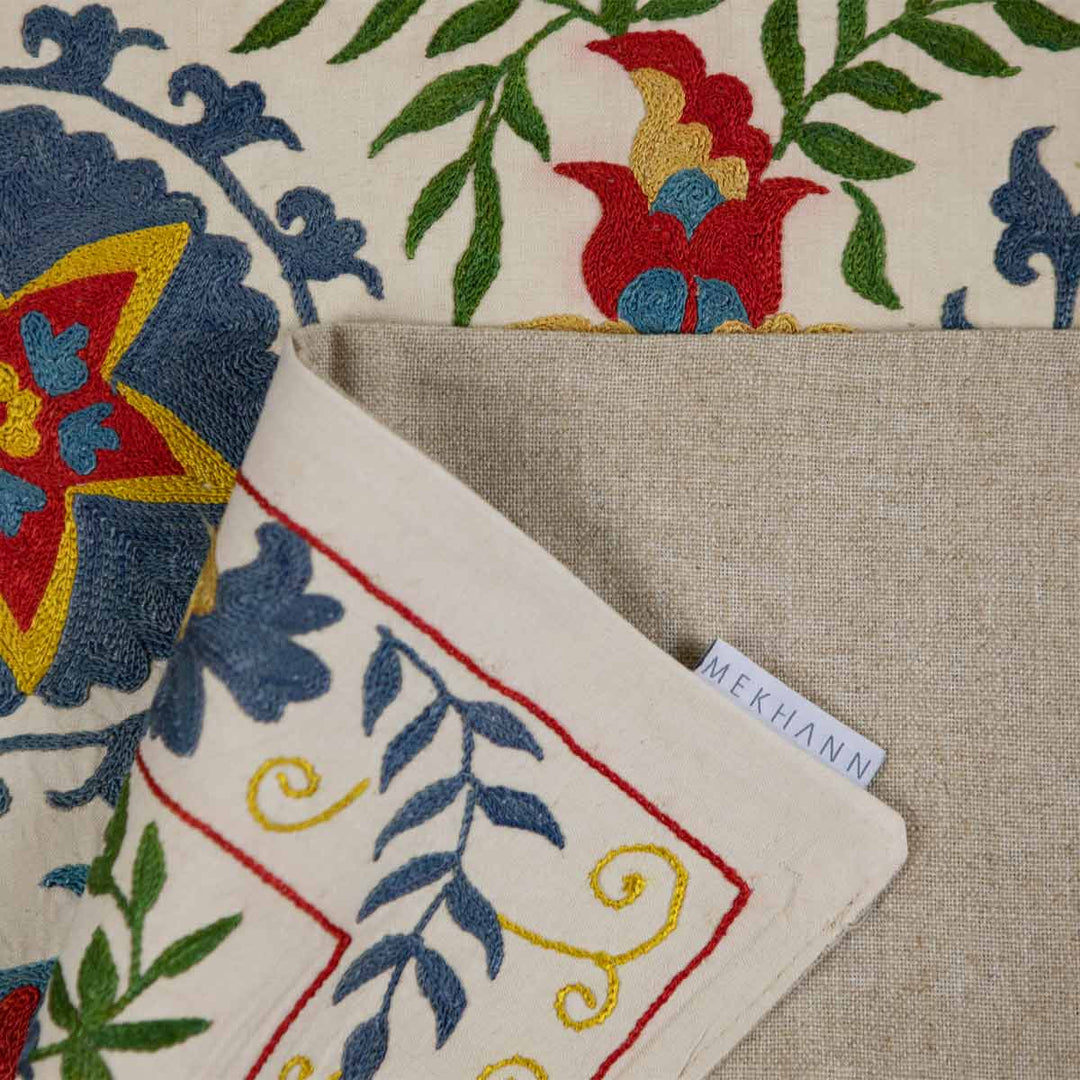 Folded view of Mekhann's cream iznik petite throw, elegantly folded to accentuate the luxurious fabric and embroidered patterns.