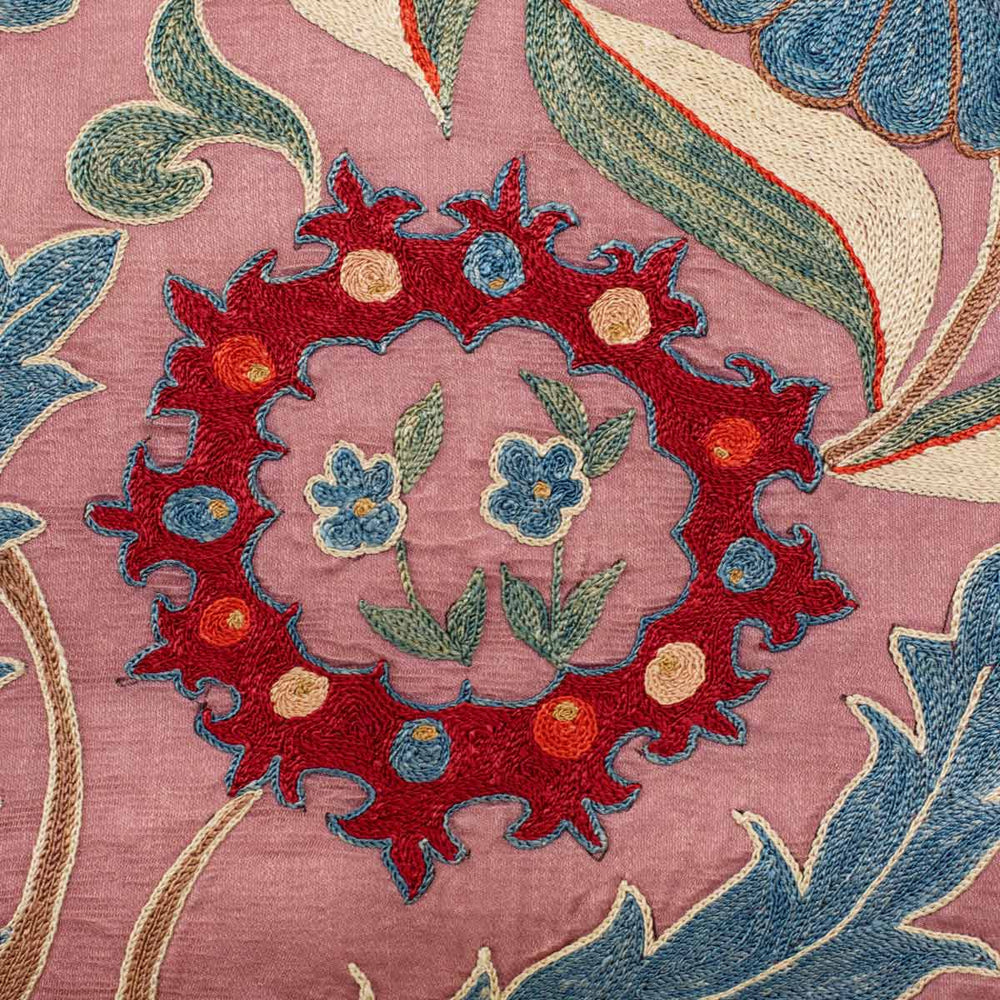 Close up view of Mekhann's violet iznik throw, displaying one of the hand embroidered silk floral motifs in bright red, with the smaller flower details in blue and green. Also revealing the texture of the violet silk base.