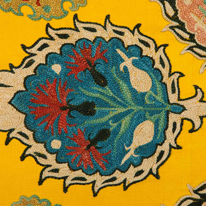 Close up view of Mekhann's yellow botanical silk embroidered artwork, focusing on the light blue and cream botanical details set against the yellow silk.