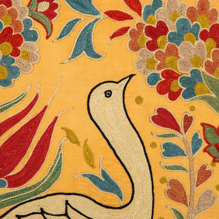 Close up view of Mekhann's yellow silk embroidered bird, with a focus on the bird's head and the subtle contrast of colours and textures in the surrounding floral embroidery.