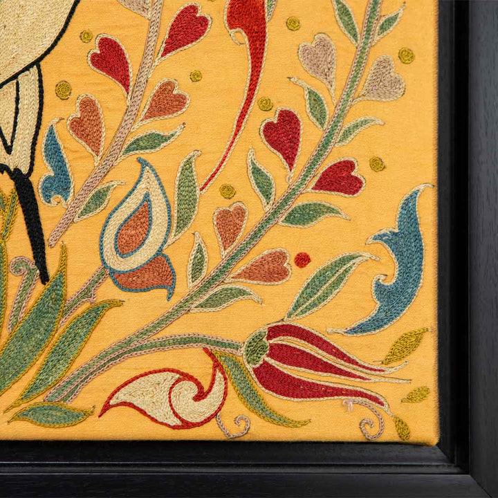Corner view of Mekhann's yellow silk embroidered bird, highlighting the corner of frame with the fine embroidery and colour gradation in the leaves and petals, set against the yellow silk fabric.