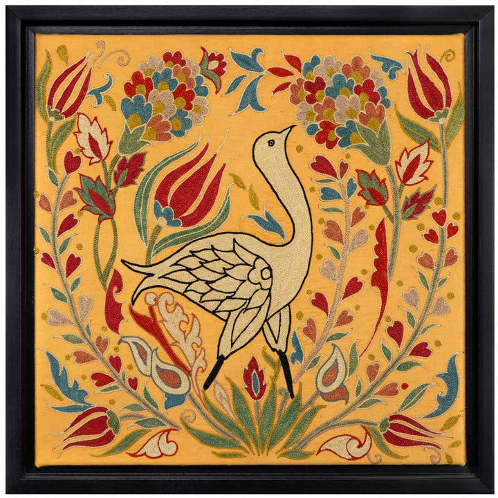 Front view of Mekhann's yellow silk embroidered bird, showcasing an embroidered bird surround by an Intricate design of vibrant florals and foliage on a silk yellow background, encased in a black frame.