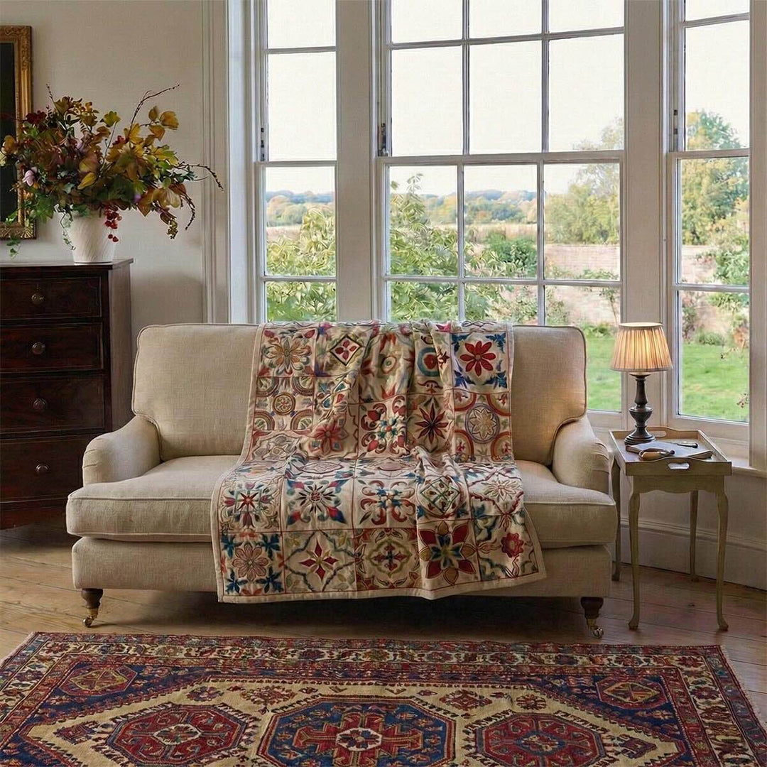 Botanical Mosaic Throw 201 draped over a cream sofa in a sunlit living room, showing embroidered mosaic panels and border detail