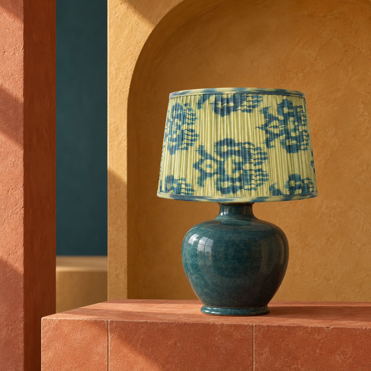 Fleur lampshade styled on a petrol ceramic base among ochre and terracotta architectural forms; illustrative editorial setting.