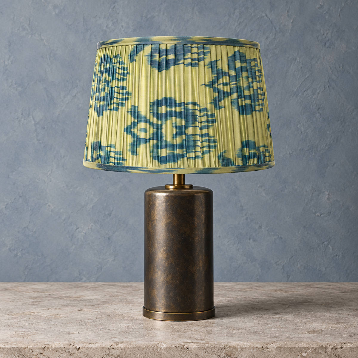 Fleur lampshade styled on a cylindrical bronze-toned base against blue-grey plaster; illustrative full-lamp portrait.