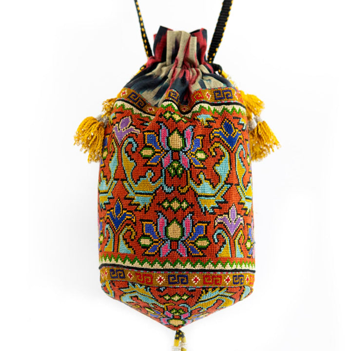 Front view of Mekhann's orange embroidered floral bucket bag, adorned with a display of traditional patterns and yellow tassel detailing.