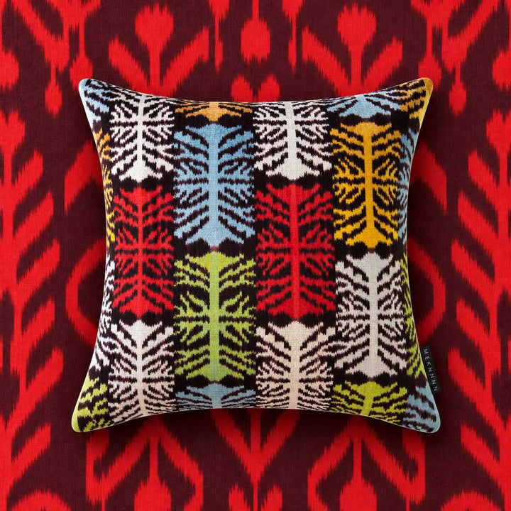 Front view of the Frond Cushion in Charcoal against a red ikat background. 