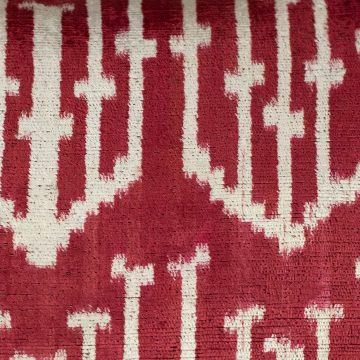 Close-up of the Spearhead motif on a handwoven silk velvet ikat cushion, highlighting the deep crimson and burgundy hues with intricate resist-dye techniques.