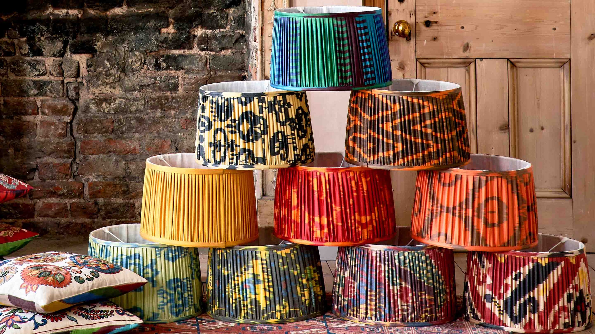 Colorful patterned lampshades stacked on a table with a rustic background.