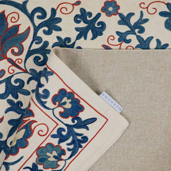 Folded view of Mekhann's cream iznik petite throw, showing the back lining fabric of the throw with the Mekhann label stitched onto the edge.
