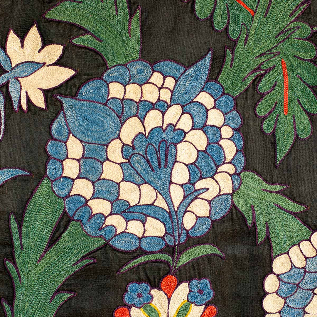 Close up view of Mekhann's black iznik throw, showing the hand embroidered floral iznik pattern in blue, white and green on the black silk base.