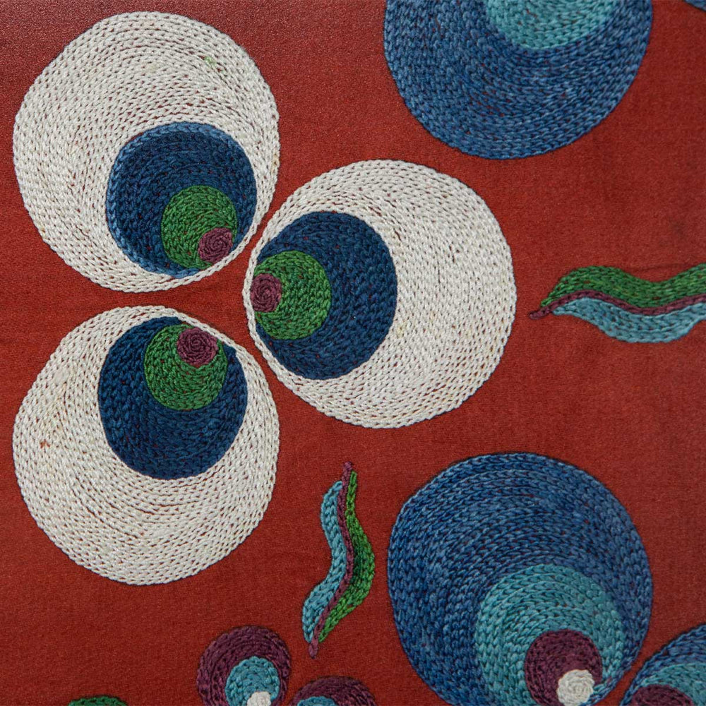 Close up view of Mekhann's light maroon silk cintamani artwork, revealing a cream, blue and green embroidered Cintamani pattern, all hand embroidered onto a base on light maroon silk.