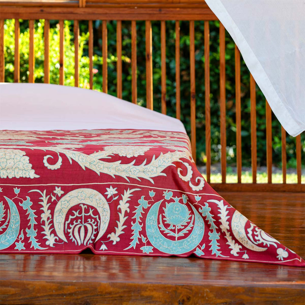 In use view of Mekhann's maroon grape vines throw, where the throw has been used as part of a bed spread and has been placed at the foot on the bed.