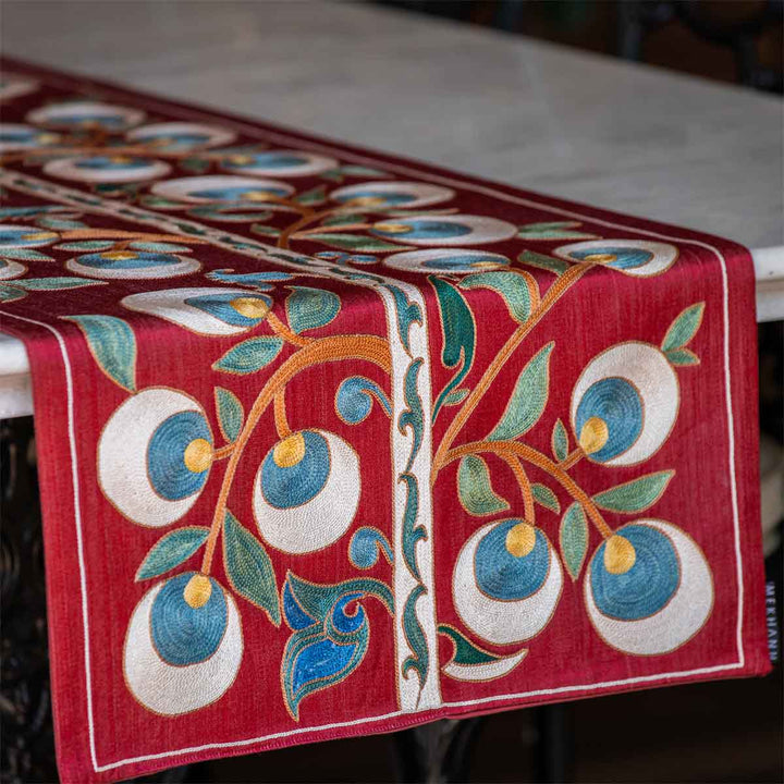 In use view of Mekhann's maroon cintamani runner, shown draped over a table with light bouncing off the bright maroon coloured silk.