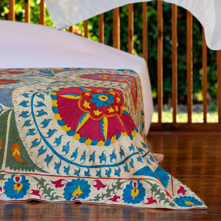 In use view of Mekhann's multicoloured medallion throw, where the throw can be seen draped over the foot of a bed spead. 