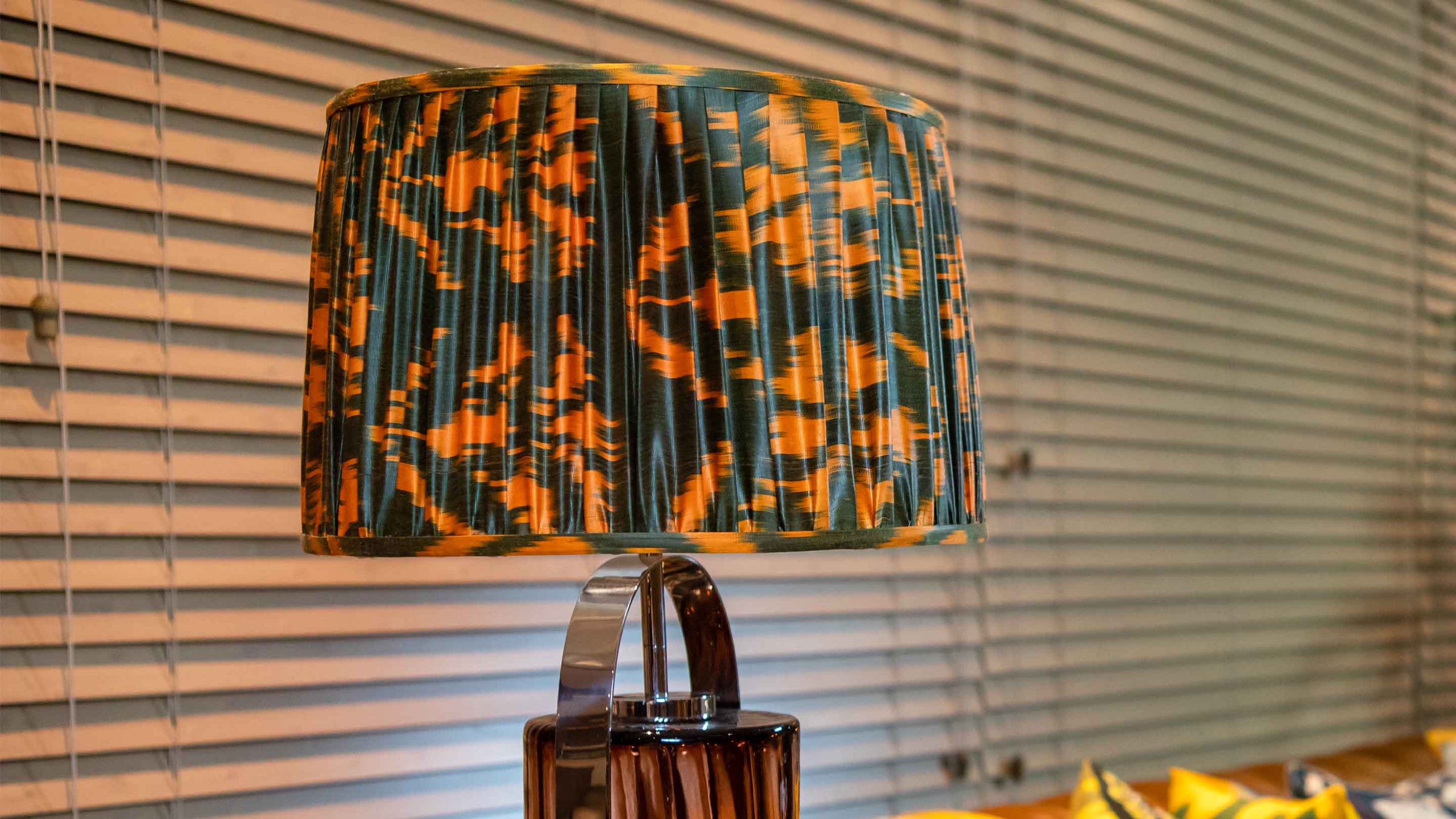 Lamp with a colorful pleated shade against a window with blinds